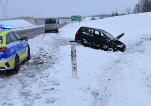 czarny samochód w zaśnieżonym rowie obok radiowóz