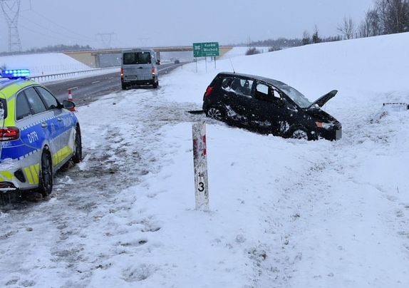 czarny samochód w zaśnieżonym rowie obok radiowóz
