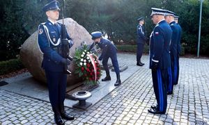 Komendanci Policji oddający honor i składający kwiaty przed tablicą pamięci