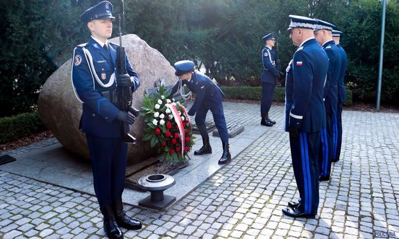 Komendanci Policji oddający honor i składający kwiaty przed tablicą pamięci