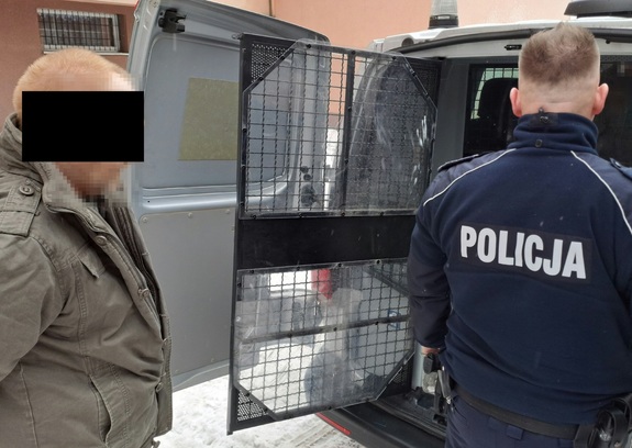 zatrzymany mężczyzna wsiadający do okratowanego busa przy którym stoi policjant