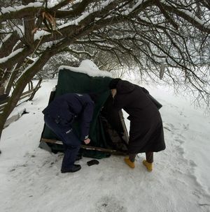 policjant i pracownica OPS zaglądający do namiotu