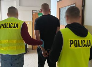 policjanci prowadzący zatrzymanego mężczyznę w kajdankach