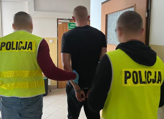 policjanci prowadzący zatrzymanego mężczyznę w kajdankach