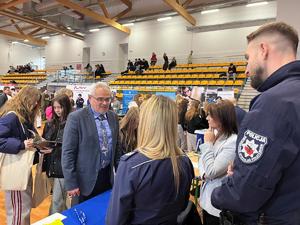 Policjant stojący przy stanowisku rozmawiający z zainteresowanymi osobami.