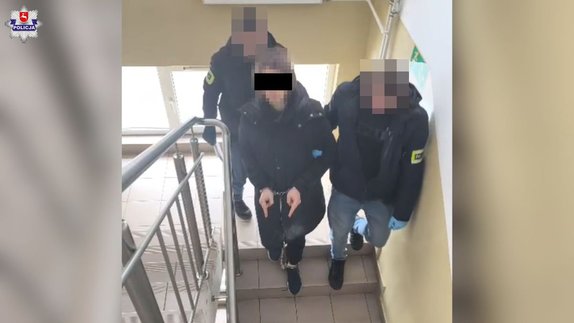 Dwóch policjantów doprowadzających zatrzymanego mężczyznę, który ma założone kajdanki.