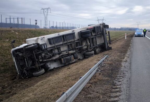 ciężarówka leżąca na boku w rowie w tle radiowóz obok niego policjant idący szosą