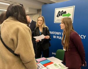 Pracownice Powiatowego Urzędu Pracy prezentujące materiały informacyjne ulotki osobom stojącym przed nimi