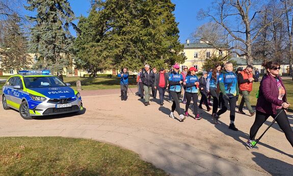 nordikowcy maszerujący obok stoi radiowóz