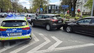 skrzyżowanie a na nim trzy stojące kolejno za sobą samochody przed nimi radiowóz obok dwóch strażaków
