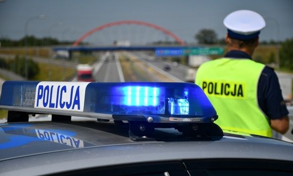 Policjant obok radiowozu patrzący na drogę