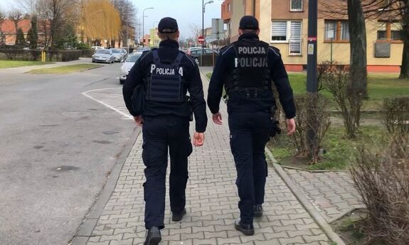 policjanci idący chodnikiem przez osiedle