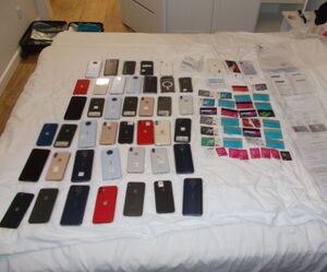 łóżko a na nim kilkadziesiąt telefonów komórkowych i kart płatniczych