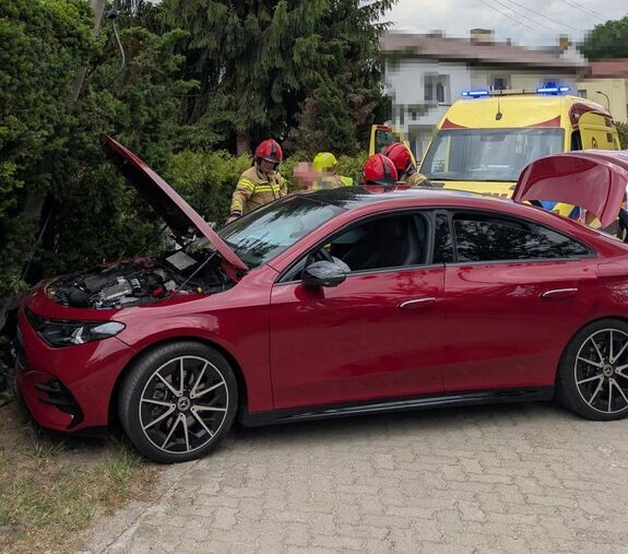 czerwony mercedes z rozbitym przodem opartym o słup w tle strażacy i karetka
