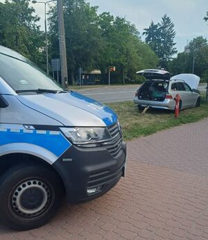fragment radiowozu policyjnego w tle srebrne BMW z otwartym bagażnikiem i podniesioną klapą