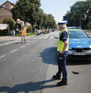 policjantka obok radiowozu patrząca na nadchodzącą pielgrzymkę