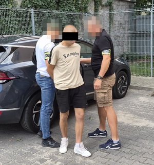 policjanci po cywilnemu z zatrzymanym mężczyzną stoją obok samochodu