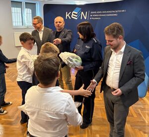 dorośli,w  tym policjantka przekazujący dzieciom kaski ochronne