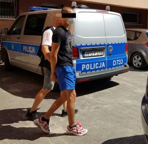 policjant prowadzi zatrzymanego, w tle widać radiowóz