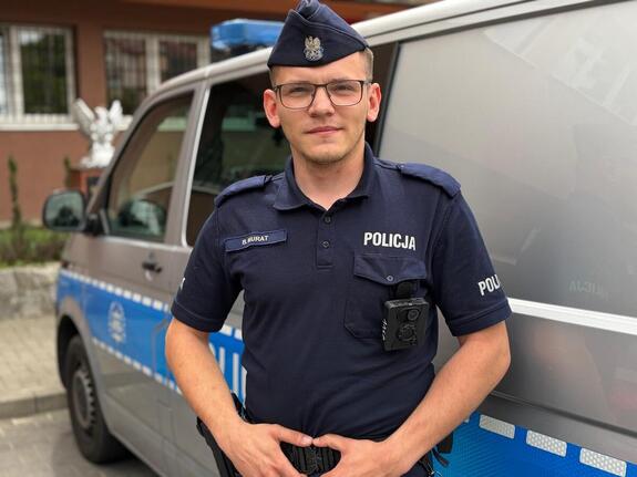 posterunkowy Bartłomiej Murat stoi przy radiowozie
